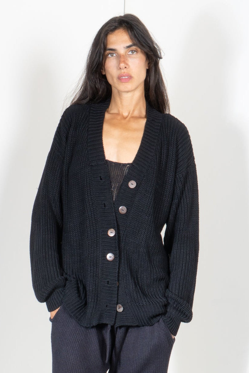 Person wearing a black knit cardigan and matching pants on a white background