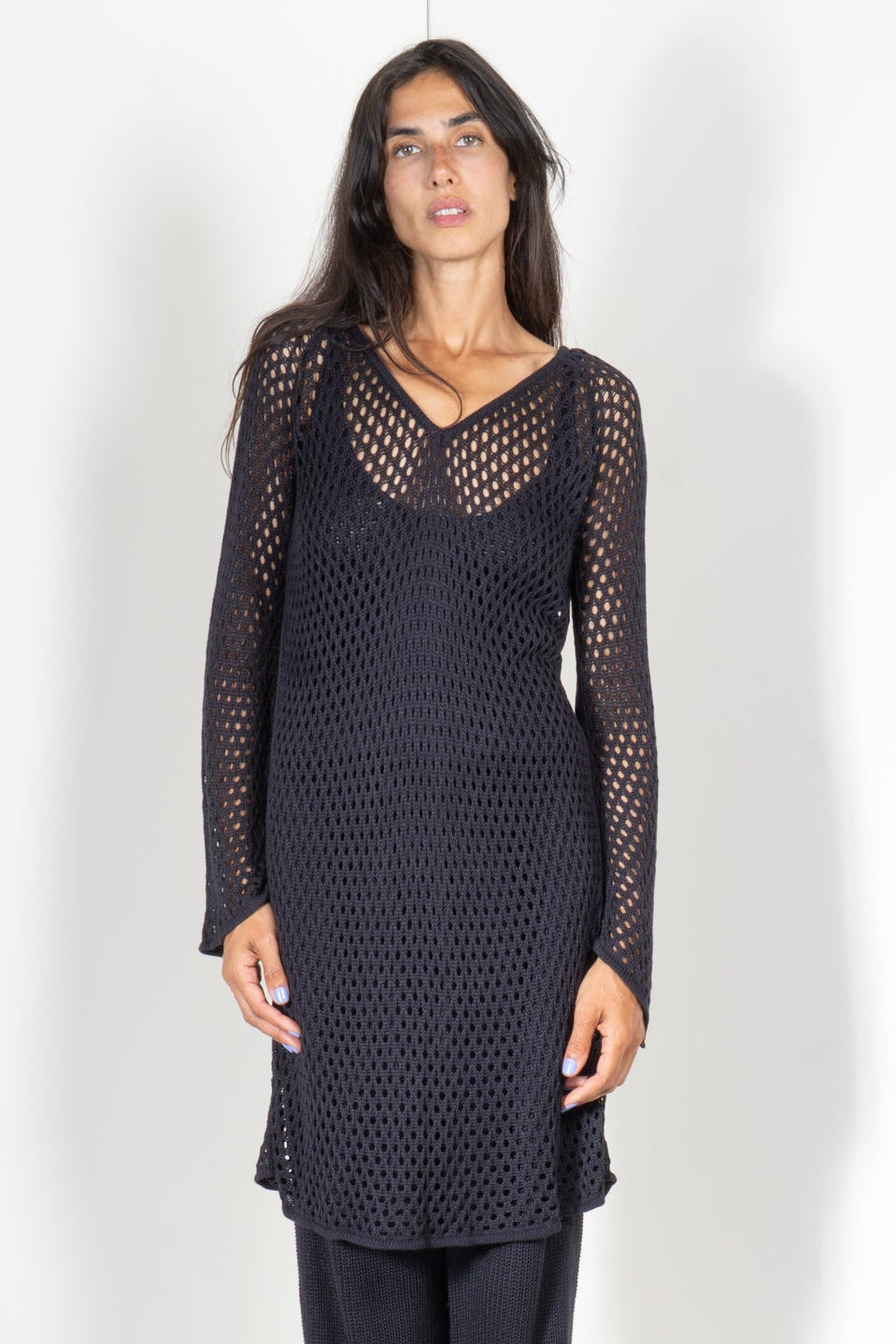 Woman wearing a black long-sleeve knit shirt dress in a eyelet mesh motif and pants on a white background